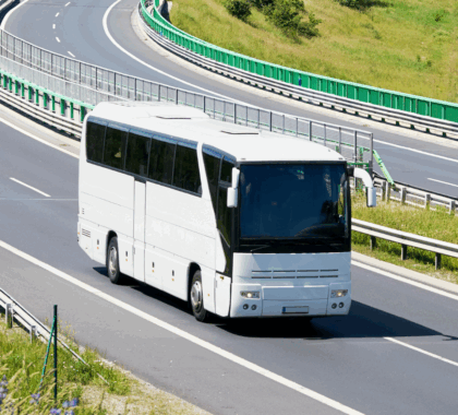 A large white commercial bus drives down the road