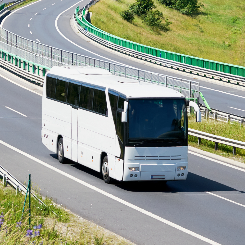 A large white commercial bus drives down the road