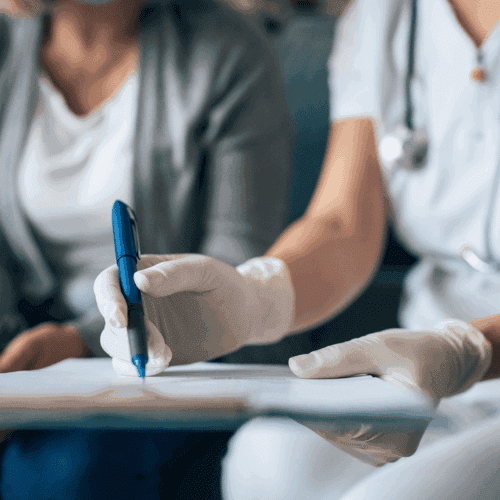 A physician reviews medical documents with a patient, holding a blue pen over the paperwork as they discuss