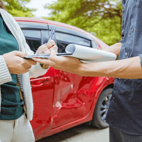 Man and woman exchanging insurance information after a car accident, a red car in the background has a dent in the side