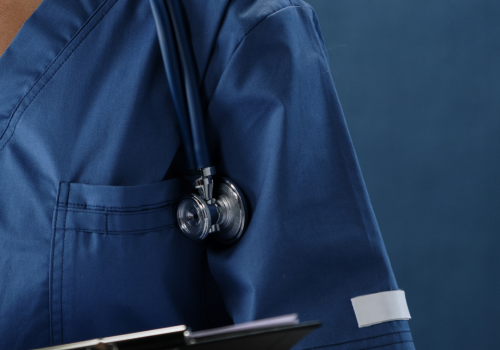 Medical professional wearing scrubs with stethoscope draped over shoulder and holding a clipboard